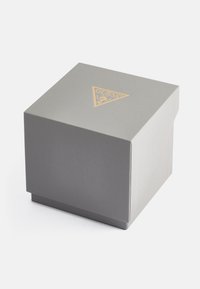 Caixa de presente cinza texturizada com um logótipo triangular dourado no topo. A caixa possui uma tampa segura e uma superfície de fundo suave.