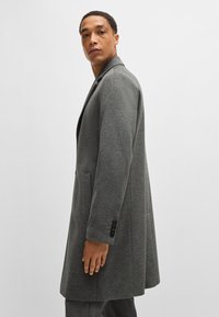 Grauer Wollmantel mit taillierter Passform, ausgestattet mit einem Reverskragen, einer Ein-Knopf-Verschluss und seitlichen Taschen. Glatte Textur mit gefüttert Innenraum.