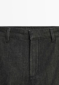 Sorte denimbukser med et tekstureret stof, der har en talje med bæltestropper og standard forlommer.