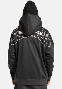 Zwarte hoodie met een groot wit gedrukt logo op de achterkant, voorzien van een geribde zoom en manchetten. De stof lijkt glad en zacht.