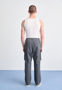 Grå cargo-bukser med elastisk midje, to sidelommer og smale ben. Båret med en hvit tanktop, sett fra baksiden.
