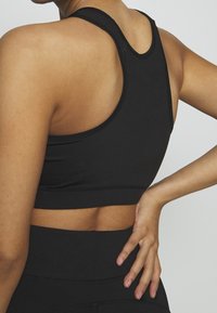 Svart sportbh med racerback-design, tillverkad av slätt material. Har sömnadsdetaljer och en åtsittande silhuett.