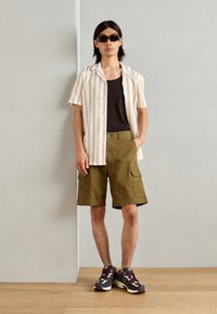 Lyhythihainen, raidallinen paita vaaleanbeige ja valkoisena, yhdistetty oliivinvihreisiin cargo-shortsit. Käytetään tummien lenkkareiden ja aurinkolasien kanssa.