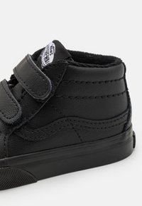 Svarte skinnhøysko med borrelåser, teksturert overflate, stikningdetaljer og gummisåle. Vans-logoetikett på toppen.