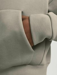 Felpa fitted a maniche lunghe di colore verde oliva con una texture morbida. Presenta una tasca frontale e polsini a costine.