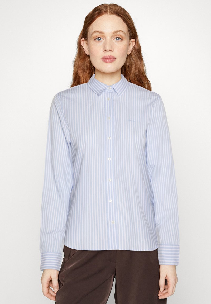 Light blue striped button-up shirt with a collar, long sleeves, and a straight hem. Fabric appears smooth with a subtle sheen.