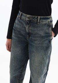 Jeans de mezclilla azul claro con un acabado desgastado, cintura alta y diseño de cinco bolsillos. Presentan un botón de metal y detalles de costura.