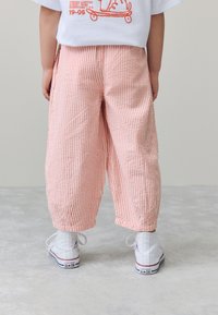Pantalon large à rayures roses et blanches, en tissu texturé, associé à des baskets montantes blanches avec un logo étoile bleu et des accents rouges.