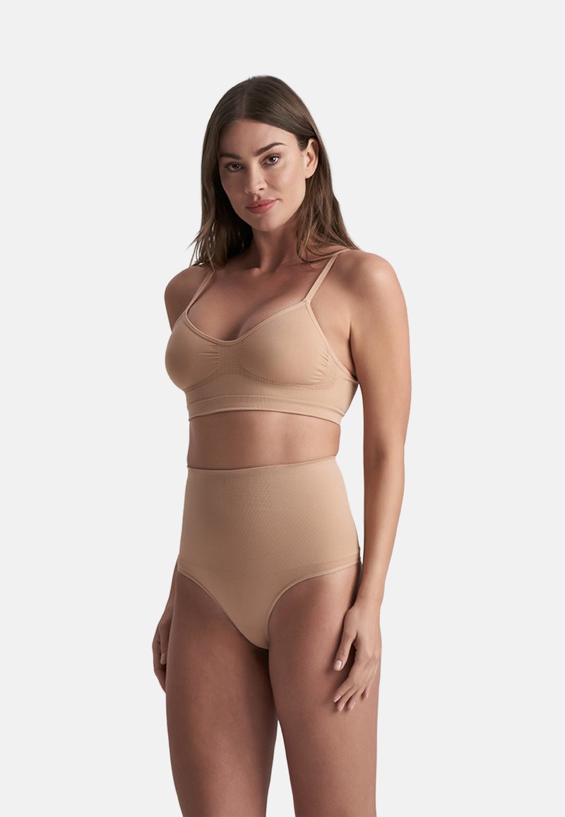 Naakte bralette met een gladde textuur en dunne verstelbare bandjes, gecombineerd met naadloze high-waisted slipjes, ontworpen voor comfort en ondersteuning.
