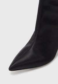 Pantof cu vârf ascuțit din satin negru, cu un design elegant, având o textură netedă și detalii subtile de cusături de-a lungul marginilor.