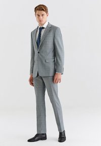 Szary kostium w kratkę o dopasowanym kroju, biała koszula wizytowa i niebieski krawat w wzory. Czółenka w kolorze czarnym dopełniają stroju.