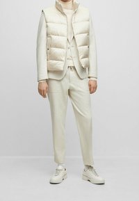 Puffer vest in light beige with a quilted design, paired with a matching soft sweater and trousers. White sneakers complete the look.
