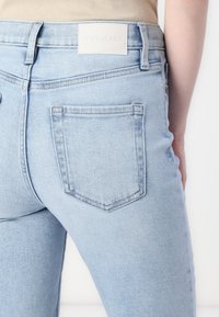 Lys blå denimjeans med en glatt tekstur, med to baklommer og en hvit etikett i midjen.