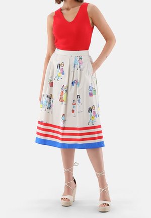 Femme portant un haut sans manches rouge et une jupe midi blanche avec des figures illustrées colorées et un ourlet rayé rouge et bleu, debout avec une main dans la poche.