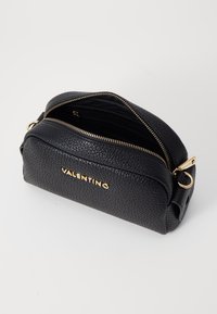 Svart läderhandväska med strukturerad yta, guldfärgade detaljer, dragkedjestängning och präglad "VALENTINO" -text på framsidan.