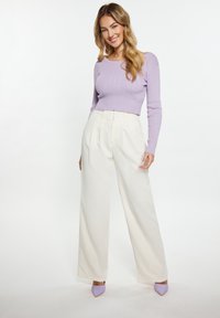 Maglione a coste di un delicato viola abbinato a pantaloni bianchi a gamba larga e tacchi color lavanda. Presenta una silhouette aderente e una texture liscia.