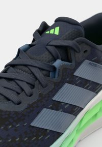 Dark blue athletic shoe featuring textured mesh upper, contrasting green accents, and three grey stripes on the side.