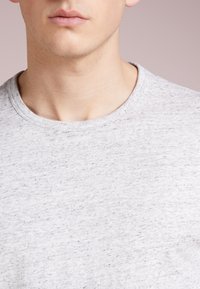 T-shirt grigio a maniche corte con collo rotondo, realizzato in un tessuto morbido e testurizzato con un motivo mélange. Senza ulteriori dettagli.