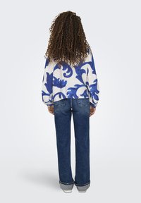 Blaues Pulloveroberteil mit floralem Muster und langen Ärmeln, kombiniert mit dunkelblauben, geraden Jeans, die am Saum einen leichtenFransen haben.