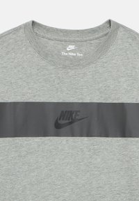 Siva kratka majica s krožnim izrezom, z vodoravno črno črto in črnim logotipom Nike, natisnjenim na sprednji strani.
