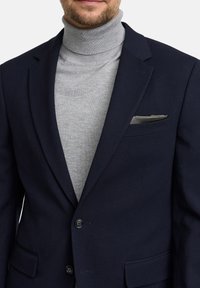 Granatowa marynarka o fakturze, zapinana na dwa guziki, noszona na jasnoszary golf. Zawiera poszetkę i widoczne detale przeszyć.