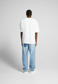 Valkoinen lyhythihainen t-paita, joka on valmistettu puuvillasta, yhdistettynä vaaleansinisiin kuluneisiin farkkuihin. Farkuissa on paikka ja rento malli.