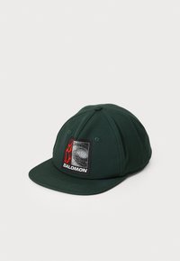 Cappello verde scuro in cotone, con una toppa rettangolare nera e rossa contenente il testo "SALOMON" sulla parte anteriore. Design con visiera piatta.
