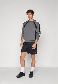 Grå genser med svarte detaljer og hvite striper på ermene, kombinert med svarte shorts. Har logo på brystet og en avslappet passform.