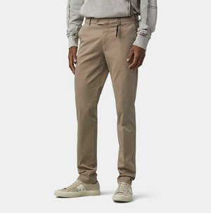 Homme portant un pantalon beige slim, des baskets beige clair, et un sweat-shirt gris clair à manches longues avec les manches remontées.