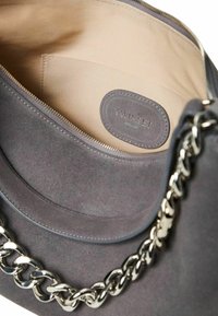 Borsa in suede grigia con interno beige, dotata di chiusura a zip e tracolla in catena argentata. L'interno include un'etichetta con il logo "TWINSET" in rilievo.