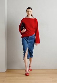 Rdeč pleten pulover, denim midi krilo s sprednjim razporkom in rdeče sandale z naramnicami, nošene z črno torbico; sodobni elementi teksturiranih tkanin.