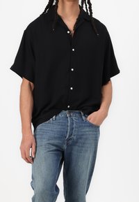 Czarna koszula z krótkim rękawem zapinana na guziki z białymi guzikami, w połączeniu z niebieskimi, wyblakłymi dżinsami. Gładki materiał i luźny krój.