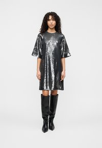 Ασημένιο φόρεμα με παγιέτες, κοντά μανίκια, άνετη εφαρμογή και στρογγυλή λαιμόκοψη. Συνδυασμένο με μαύρες μπότες μέχρι το γόνατο από λείο δέρμα.