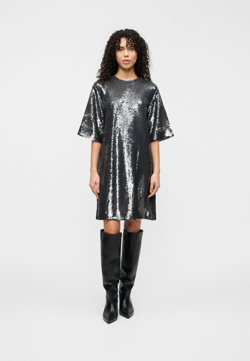 Ασημένιο φόρεμα με παγιέτες, κοντά μανίκια, άνετη εφαρμογή και στρογγυλή λαιμόκοψη. Συνδυασμένο με μαύρες μπότες μέχρι το γόνατο από λείο δέρμα.