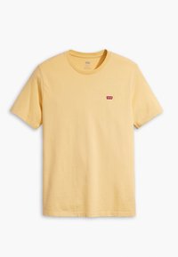 Żółta bawełniana koszulka z krótkim rękawem i okrągłym dekoltem. Posiada małe czerwone logo Levi's po lewej stronie klatki piersiowej. Gładka faktura.