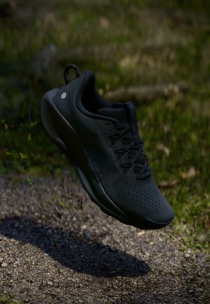 Black athletic shoe with a textured mesh upper, lace closure, and a cushioned sole. Features a streamlined design and a reflective logo detail.