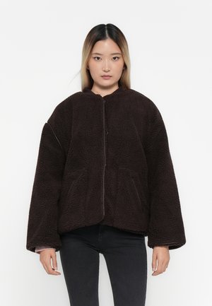 Veste en polaire brune et moelleuse avec col rond, manches longues et poches avant. Elle présente une fermeture éclair et une surface texturée.