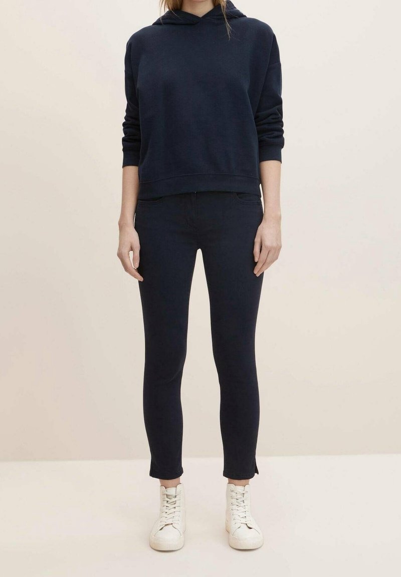 Navy blue hoodie with a relaxed fit and a kangaroo pocket, paired with dark jeans and white sneakers; smooth fabric with minimal stitching.