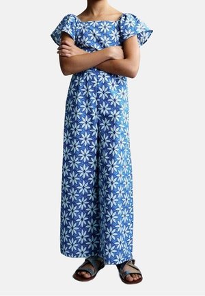 Robe à motifs floraux bleus avec de courtes manches volantées, de longueur longue et une coupe décontractée, associée à des sandales brunes.