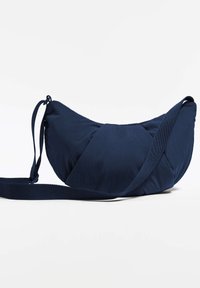 Sac bandoulière bleu marine en tissu doux et matelassé. Présente une forme courbe et asymétrique ainsi qu'une bandoulière réglable pour plus de confort.