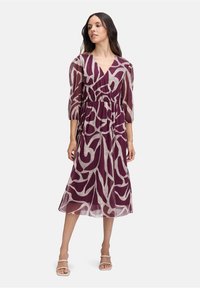 Vestito midi avvolgente in tessuto trasparente color bordeaux con motivo astratto beige. Presenta maniche a sbuffo e una vita elasticizzata. Scarpe: con cinturini chiari.