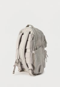 Ανοιχτό γκρι επενδυμένο σακίδιο πλάτης με πολλαπλές θήκες με φερμουάρ και ρυθμιζόμενους ιμάντες ώμου, εμφανίζεται όρθιο σε λευκό φόντο.