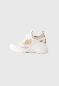Sneaker a maglia bianca e beige con suola chunky, lacci anteriori, logo del marchio sul lato e linguetta sul tallone su sfondo uniforme.