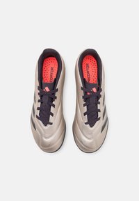 Scarpe da calcio sintetiche beige con lacci scuri, dettagli neri e tomaia testurizzata. Sottopiedi arancioni brillanti con marchio "PREDATOR". Design della punta arrotondato.