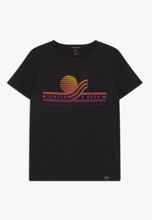 Sort t-shirt med korte ærmer med en solnedgangsgrafik og teksten "Scotch & Soda Amsterdam Couture" i gradient orange og pink toner foran.