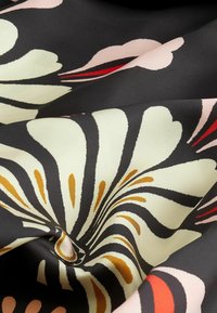 Gepatineerde stof toont een bloemmotief in crème, oranje en rood op een zwarte achtergrond. De textuur lijkt glad en zijdeachtig.