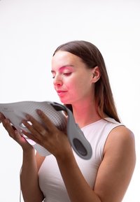 LED ansiktsmask i vitt med en mjuk textur, utrustad med ett handtag och synliga ljuselement, som appliceras på ansiktet för hudvård.