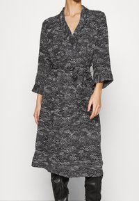 Svart och vit mönstrad omlottklänning med trekvartsärmar, bälte i midjan och knälång fåll, tillverkad av mjukt, strukturellt tyg.