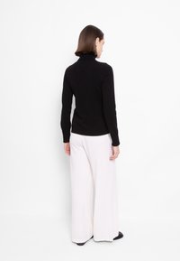 Črna turtleneck pulover z rebrastimi manšetami in robom, v kombinaciji s širokimi belimi hlačami iz mehkega materiala. Gladka tekstura, minimalističen dizajn in brez vzorcev.