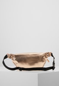 Marsupio in rose gold metallico realizzato in materiale sintetico testurizzato, con una cintura regolabile nera e chiusura con zip.